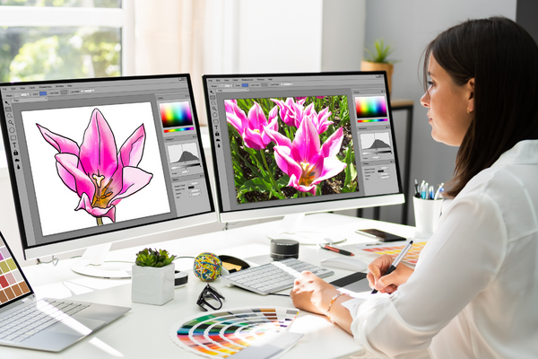 person sitting in front of two computer screens doing graphic design